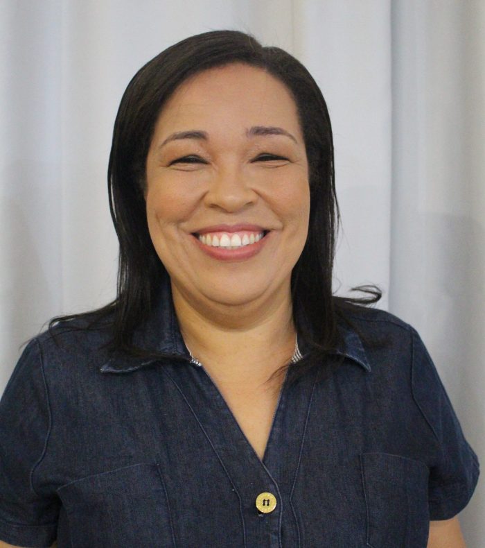 vaninha abub nordeste Vaninha, assessora da ABUB Nordeste, sorri para a foto com cabelo solto, blusa escura e na frente de um fundo neutro claro.