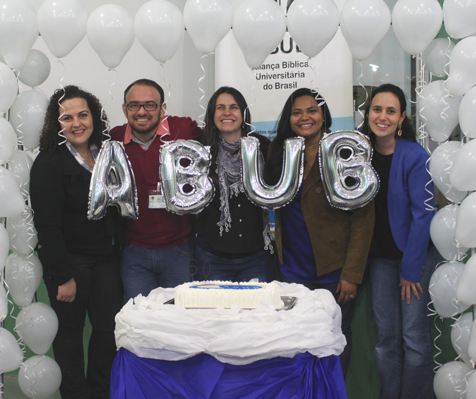 Cinco participantes da Secretaria Executiva da ABUB diante de bolo e siglas da ABUB