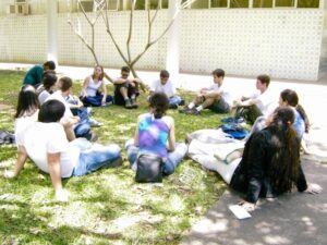 Estudantes em círculo, sentados num granado durante encontro bíblico no campus universitário