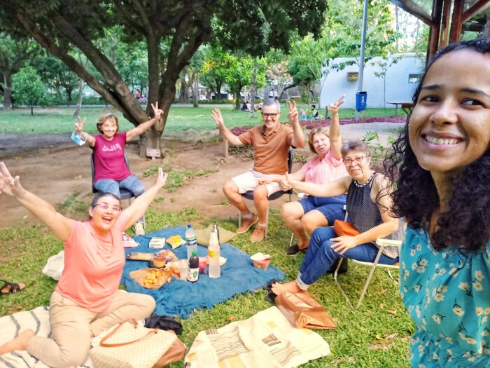 abp recife abril 2023 (1) Seis adultos sorriem e posam para a foto em um parque. Eles levantam os braços animados. No chão, sobre a grama, um pano com alimentos de piquenique. Ao fundo se vê árvores.