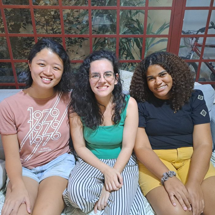 Siga-me-2023-Sayuri-Sarah-Thais Três meninas sentadas, sorriem para a foto. São as participantes do Siga-me 2023, olhando para a câmera. Elas vestem roupas informais e coloridas. A primeira é asiática, a segunda branca e a terceira negra.